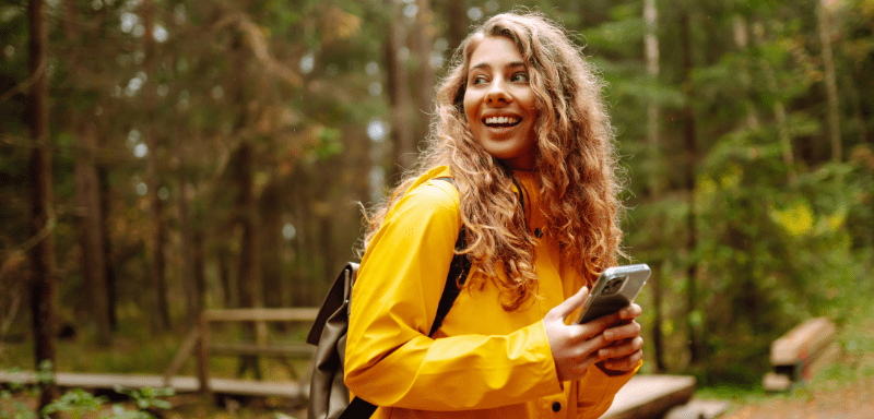 Traveler woman in the middle of nature, with her cell phone, smiling.